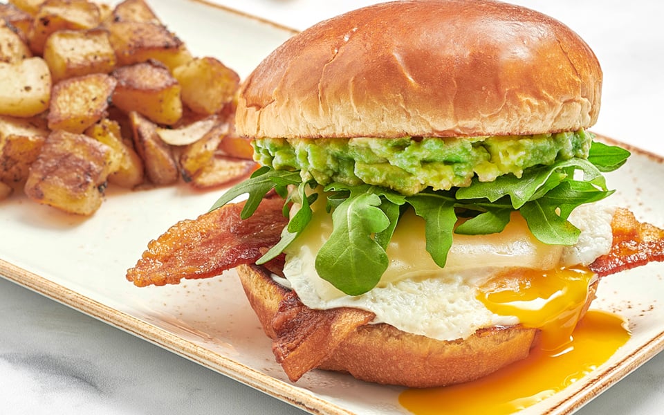 Bacon, an over-easy cage-free egg, Gruyere cheese, fresh smashed avocado, mayo and lemon-dressed arugula on a brioche bun with a side of fresh, seasoned potatoes.