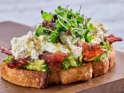 Griddled, thick-cut sourdough with fresh smashed avocado, creamy burrata filling and Million Dollar Bacon. Topped with EVOO, microgreens, cracked black pepper and fresh herbs. Served with two basted cage-free eggs and lemon-dressed organic mixed greens.
