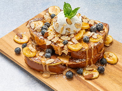 Thick-cut, custard-dipped, griddled challah bread topped with a drizzle of almond butter crème anglaise, caramelized bananas, fresh blueberries, whipped cream, honey roasted almonds, Maldon sea salt and mint. Lightly dusted with powdered cinnamon sugar.