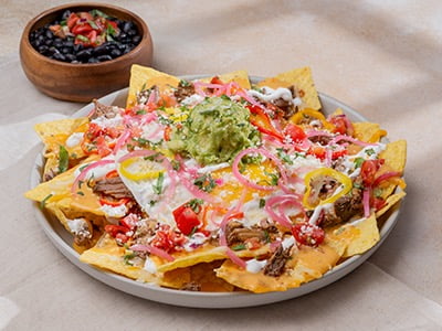 Yellow corn tortilla chips topped with melted Cheddar and Monterey Jack, braised beef barbacoa, chipotle queso and lime crema. Topped with two cage-free eggs any style, fresh smashed avocado, house-pickled red onions and sweet peppers, cilantro, housemade pico de gallo and Cotija cheese. Served with a side of seasoned black beans.
