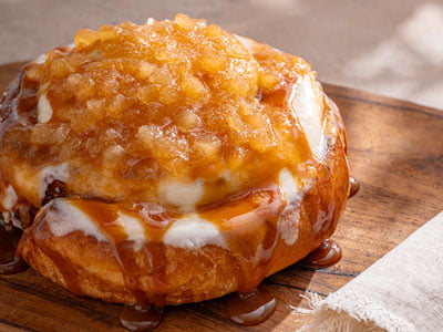 A freshly baked cinnamon roll glazed with cream cheese frosting, topped with spiced apple compote and drizzled with salted caramel.