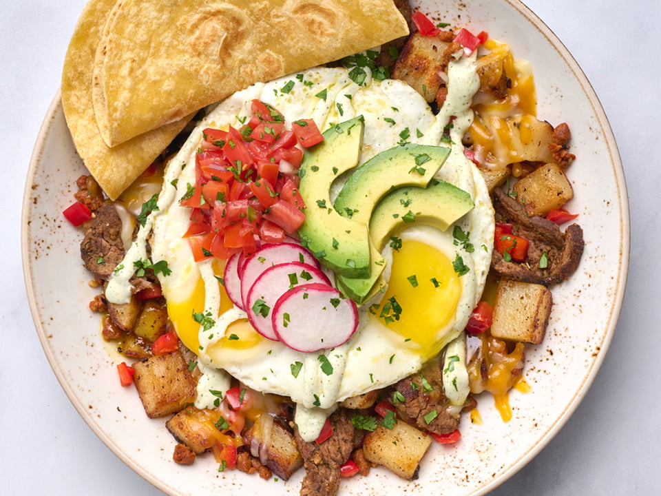 Thinly sliced carne asada, crumbled chorizo and diced red bell peppers in a potato hash topped with two cage-free eggs any style, Cheddar and Monterey Jack, housemade pico de gallo, fresh avocado, shaved radish, cilantro and jalapeño crema. Served with two warm wheat-corn tortillas.