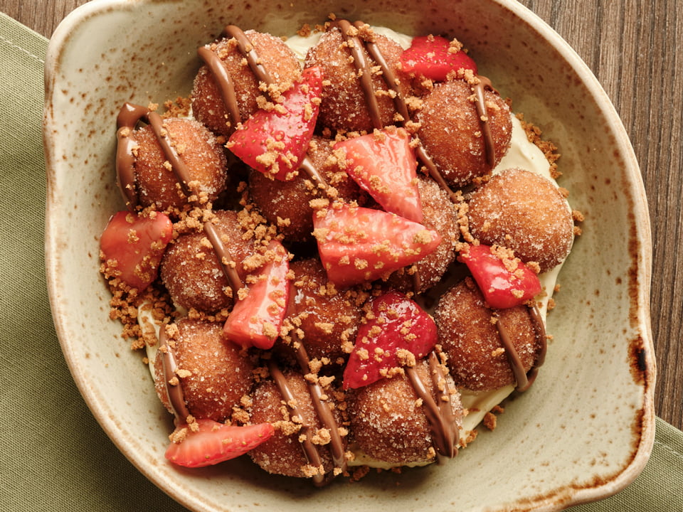 Cinnamon sugar-dusted cake donut holes served over whipped cheesecake filling then drizzled with NUTELLA® and topped with glazed strawberries, spiced gingerbread cookie crumbles and powdered cinnamon sugar.