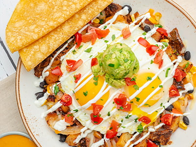 Carne asada steak, house-roasted corn and onions, Cheddar, Monterey Jack and seasoned black beans in a potato hash. Topped with two cage-free eggs any style, fresh smashed avocado, housemade pico de gallo, lime crema and cilantro. Served with two wheat-corn tortillas and a side of chipotle queso.