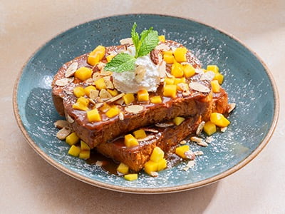 Thick-cut, custard-dipped, griddled challah bread topped with diced mango, lemon whipped cream, honey-roasted almonds and a drizzle of mango sea salt caramel sauce. Lightly dusted with powdered cinnamon sugar and garnished with mint.