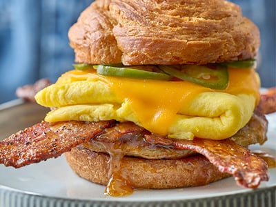 Million Dollar Bacon, a Jones Dairy Farm all-natural pork sausage patty, folded cage-free eggs, house-pickled jalapeños, aged Cheddar and bacon apricot jam on a griddled, buttery croissant round. Served with freshly seasoned potatoes.