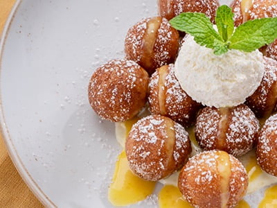 Sugar-dusted cake donut holes served over sweet cream then topped with passion fruit whipped cream and a drizzle of passion fruit curd. Lightly dusted with powdered cinnamon sugar and garnished with mint.