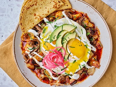 Seasoned braised beef barbacoa, house-roasted onions and Cheddar and Monterey Jack in a potato hash, topped with two cage-free eggs any style, guajillo chile consommé, lime crema, fresh avocado, house-pickled red onions and cilantro. Served with two warm wheat-corn tortillas.