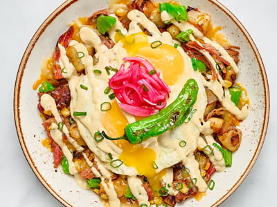 Blistered shishito peppers and smoked, hand-pulled brisket in a potato hash, topped with two cage-free eggs any style, house-roasted summer sweet corn, Cheddar and Monterey Jack, house-pickled red onions, scallions, roasted garlic aioli and Maldon sea salt.