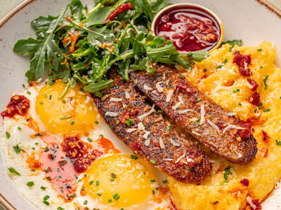 Griddled Italian pork sausage, two cage-free eggs any style and Bob’s Red Mill seasoned grits topped with lemon-dressed arugula, fresh herbs and freshly grated Parmesan. Served with a side of Calabrian chili oil.