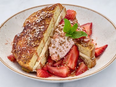 Thick-cut, custard-dipped challah bread griddled and topped with fresh strawberries, whipped cheesecake, guava cream, spiced gingerbread cookie crumbles and mint. Lightly dusted with powdered cinnamon sugar.