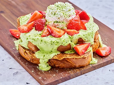 Thick-cut, custard-dipped, griddled challah bread topped with matcha crème, fresh glazed strawberries and lemon whipped cream. Lightly dusted with matcha powdered sugar and garnished with mint.