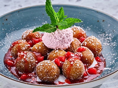 Cinnamon sugar-dusted cake donut holes served over sweet cream then topped with strawberry puree, strawberry whipped cream, pearled sugar and garnished with mint.