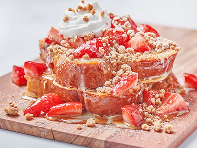 Thick-cut, custard-dipped challah bread griddled and topped with fresh strawberries, sweetened condensed milk, warm dulce de leche, whipped cream and spiced gingerbread cookie crumbles. Lightly dusted with powdered cinnamon sugar.
