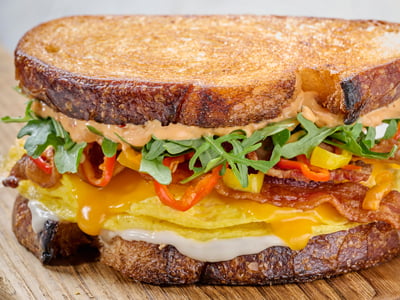 Bacon. Egg. Cheddar. Our twist on a traditional breakfast sandwich - hardwood smoked bacon, folded cage-free eggs, aged Cheddar, house-pickled sweet peppers and arugula with Calabrian chili aioli and roasted garlic aioli on griddled sourdough bread. Served with lemon-dressed organic mixed greens.