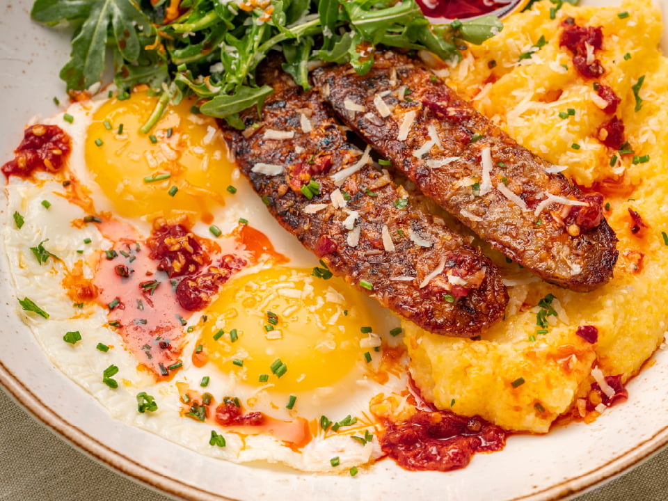 Griddled Italian pork sausage, two eggs, and seasoned grits topped with arugula and Parmesan, served with a side of chiles.
